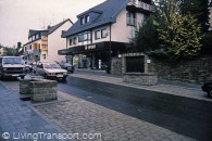 36. Much (East of Cologne, Germany) National (Federal) road passing through village carrying 6,000 vehicles per day of which 6-9% heavy vehicles. No by-pass is planned. At village centre with shops space between buildings is as little as 7 metres. Over this stretch, the carriageway has been narrowed to 4.5 metres (the narrowest on any Federal road). Two cars can pass, but large vehicles must wait for other vehicles to clear before passing through. Sight lines are arranged to enable this to happen. The low stone walls are an integral design feature of the village scheme.